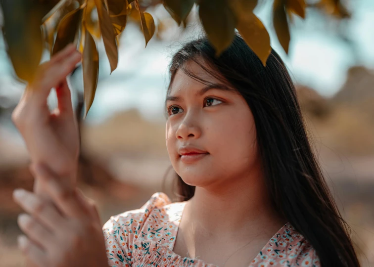 a girl standing by a tree reaching for a leaf