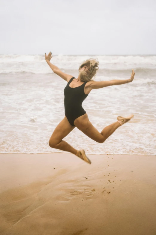 a woman jumping on the beach with her legs out in the air