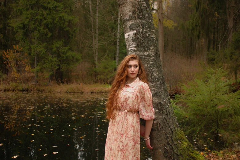 a woman stands next to a tree in the woods