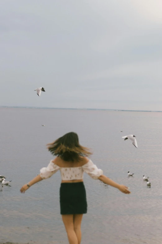 a woman is running along the shore of a large body of water with seagulls flying in the distance