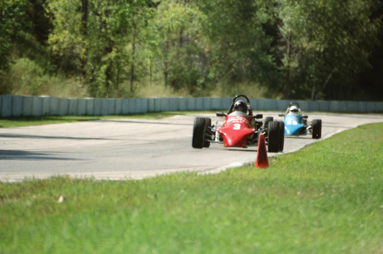 two people in an old school race car racing down a track