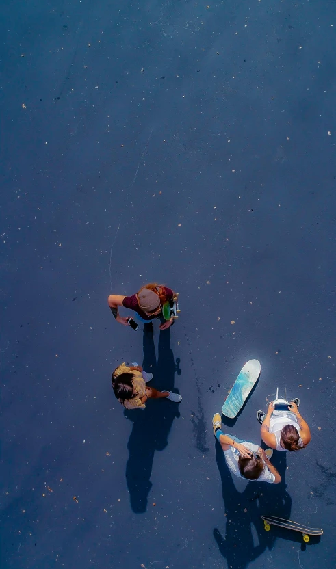 three skateboarders stand and relax on an asphalt surface