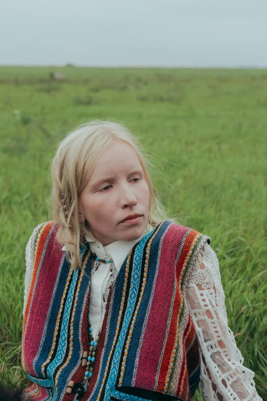 a  is sitting in the grass wearing a colorful vest