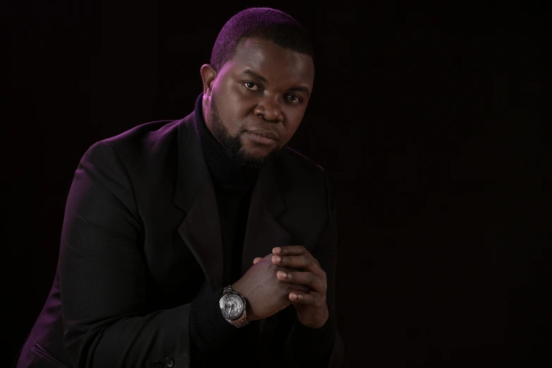 a man with dark hair wearing a black blazer sitting on a couch