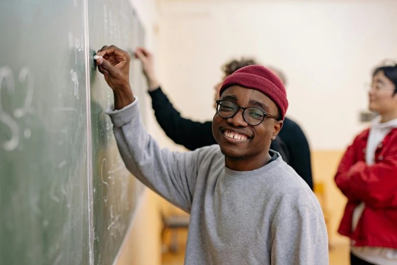 a man smiles while leaning against a chalkboard