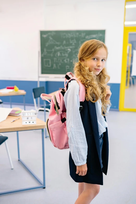 a girl is standing in a school classroom wearing a backpack and dress