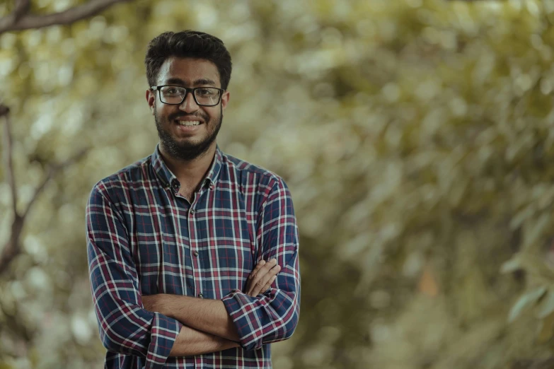 a smiling man wearing glasses next to trees