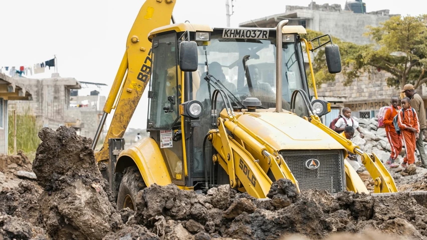 people stand next to a yellow construction vehicle in dirt