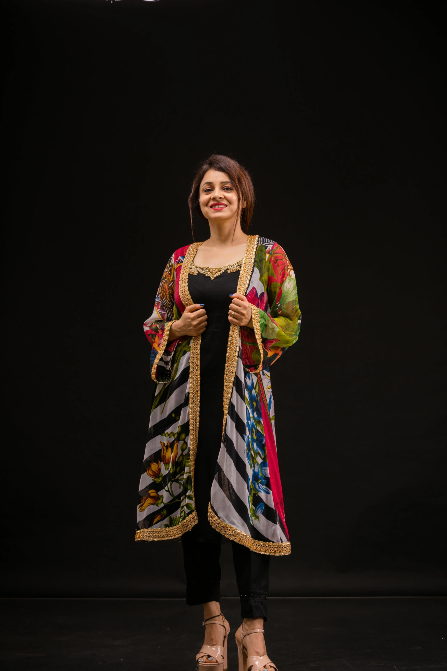 a woman in a colorful, floral dress stands in front of a black backdrop