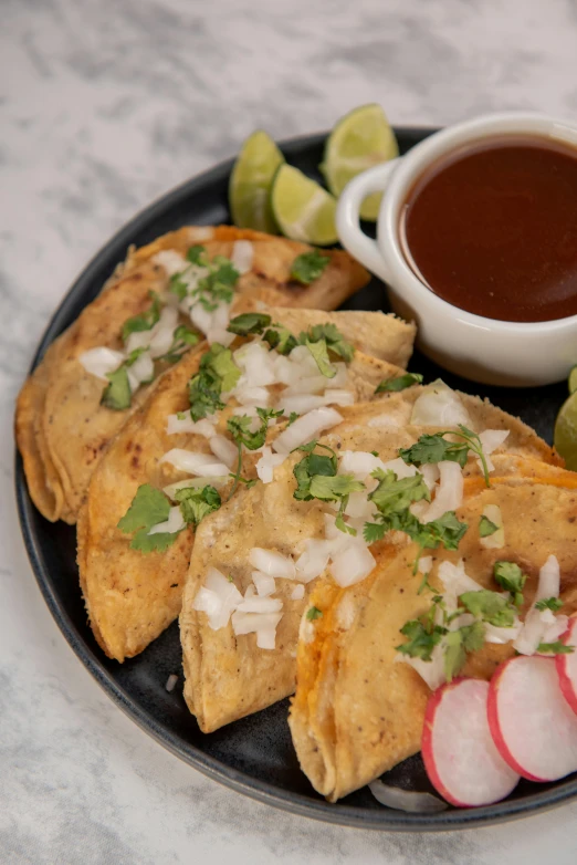 tortillas topped with onions and green onion sit on a plate next to a cup of salsa