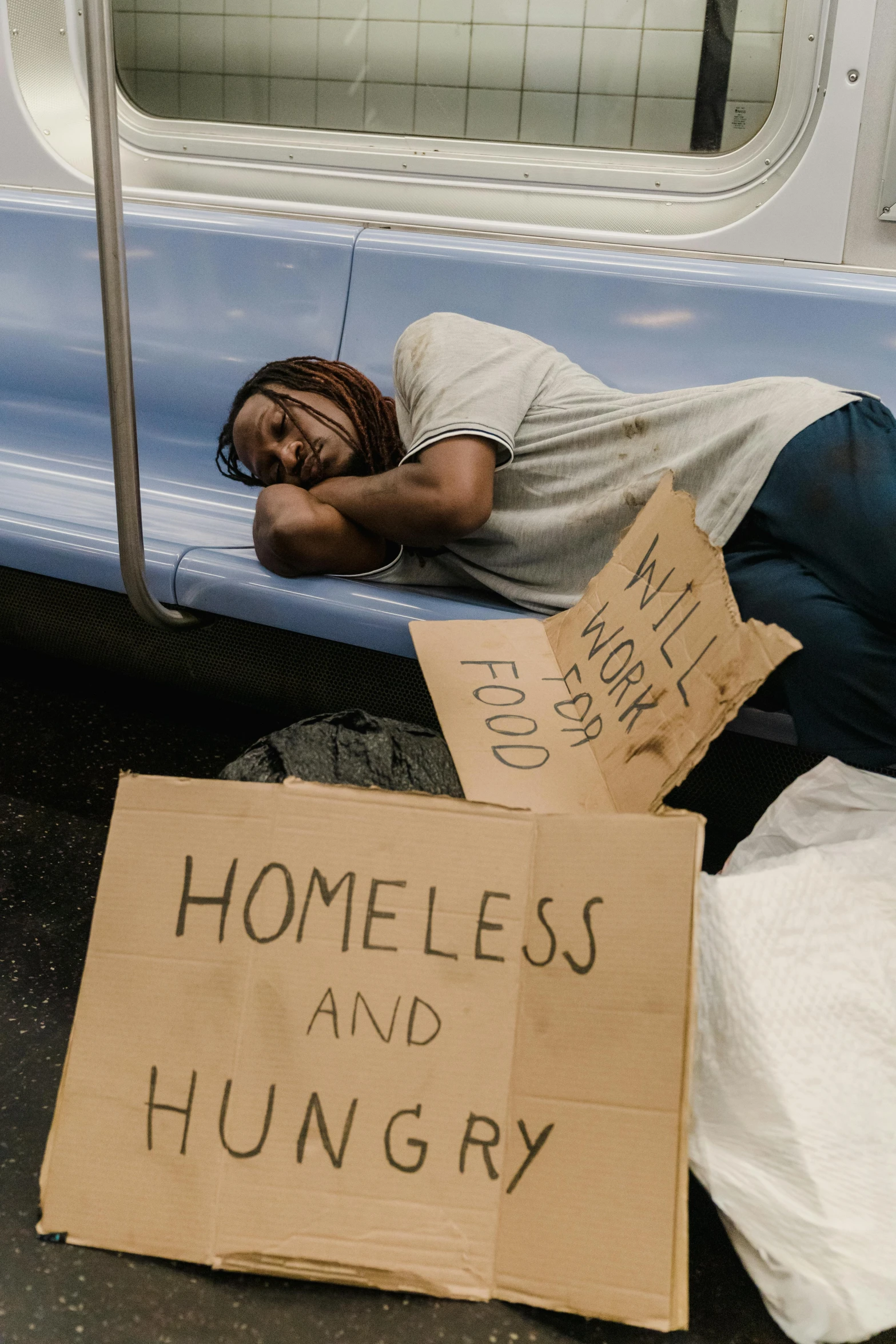 a homeless man sleeping on the bus with his head propped up against a sign