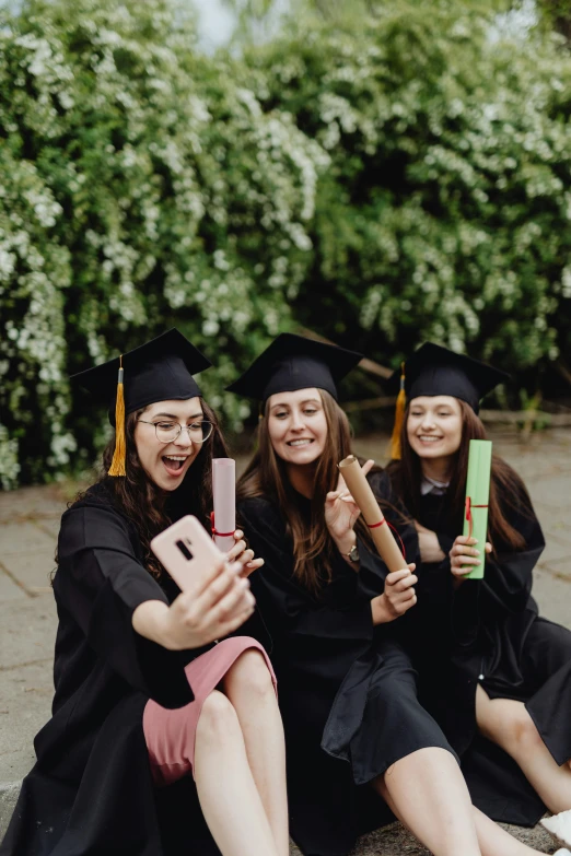 five smiling female graduates take pictures with their phones