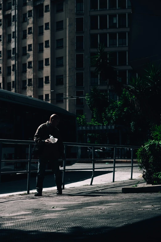 a man stands at a curb near a bus and fence