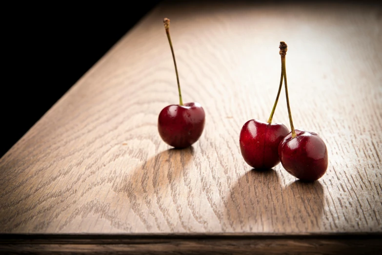 three cherries sitting on a wood table with the stem still intact