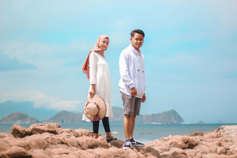 a man and woman in white standing on rocks at the beach