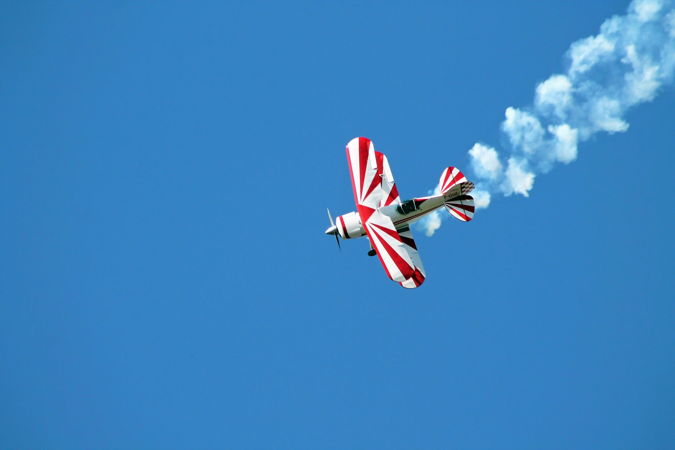 a small red and white propeller plane with smoke coming from its wings