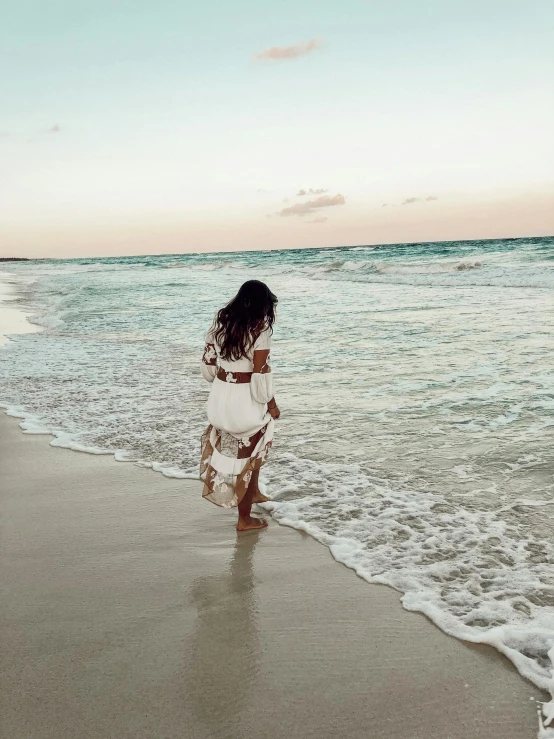 a woman stands on the beach looking into the water