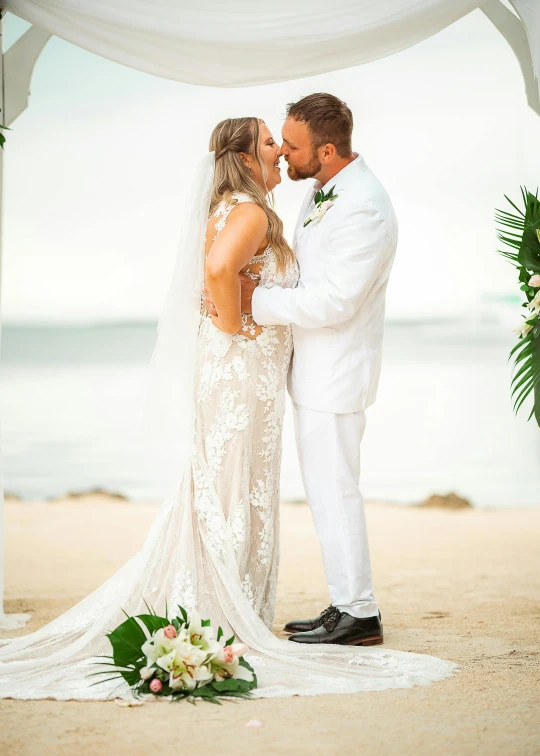 bride and groom kissing on the beach under a white dd chute