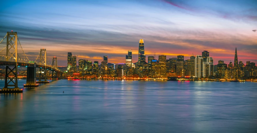 the city is in twilight with a lit up bridge over the water