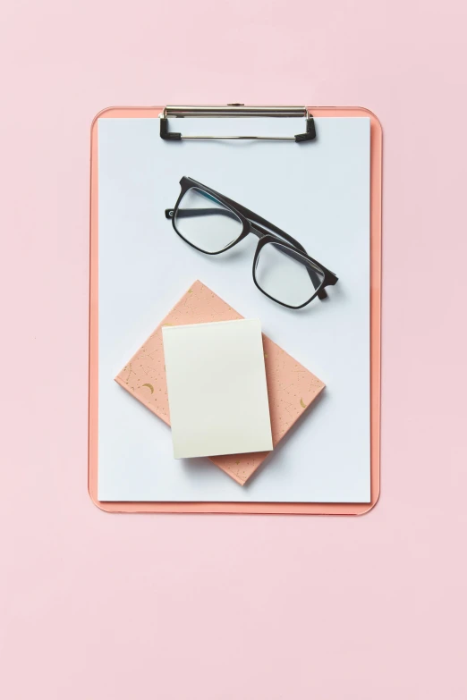 an open clipboard with glasses, a white card and a small pink dot