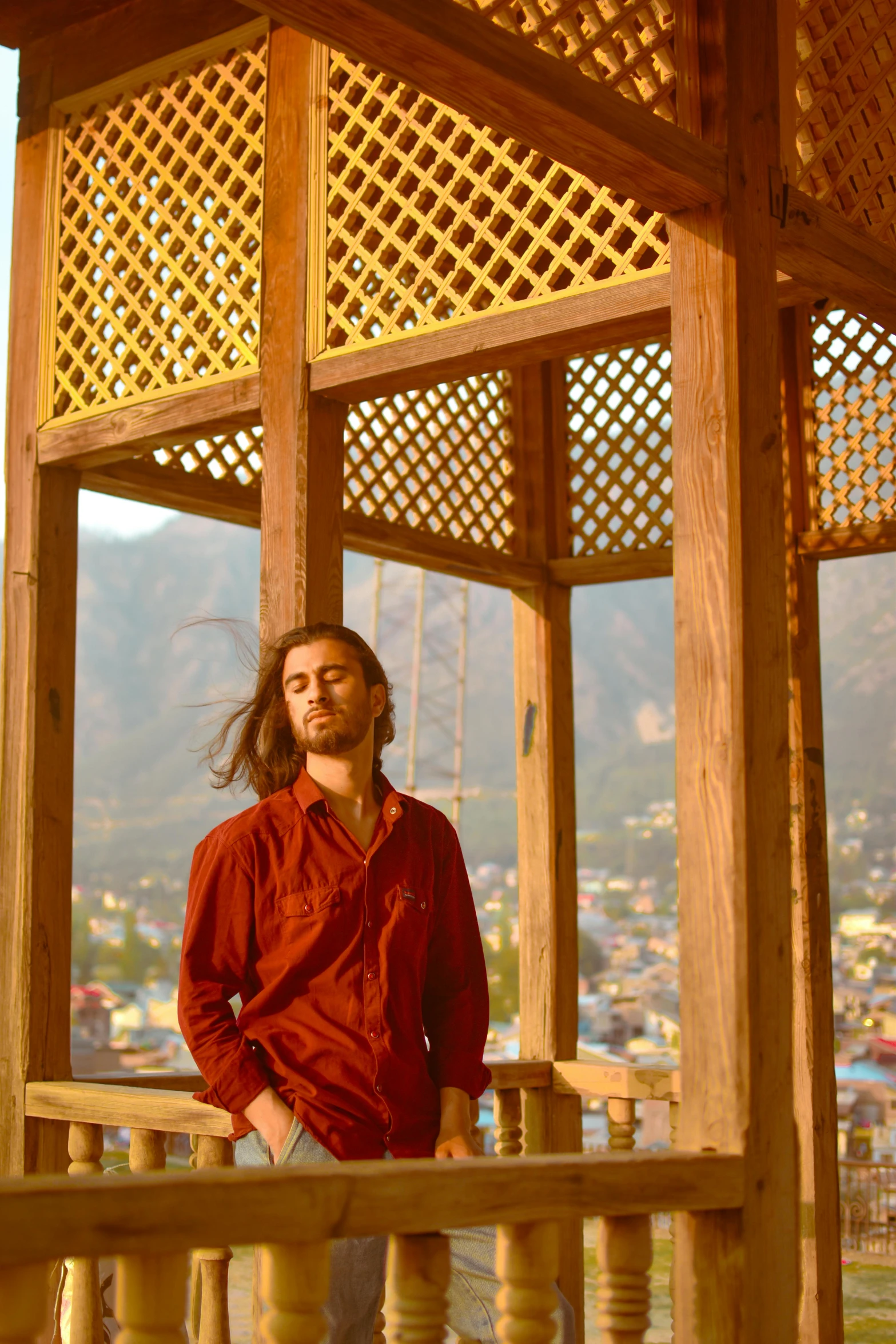 a man standing under a wooden structure with the view of mountains