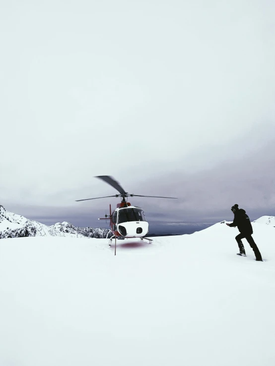 a man is standing outside in the snow near a helicopter