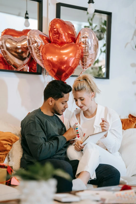 a man and woman sitting on a couch next to a birthday balloon