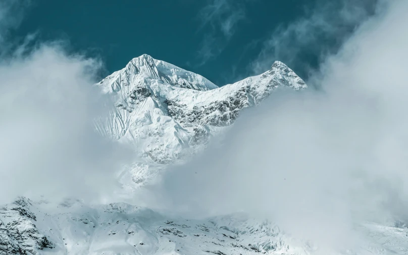 a mountain top with snow on it, with clouds in the air