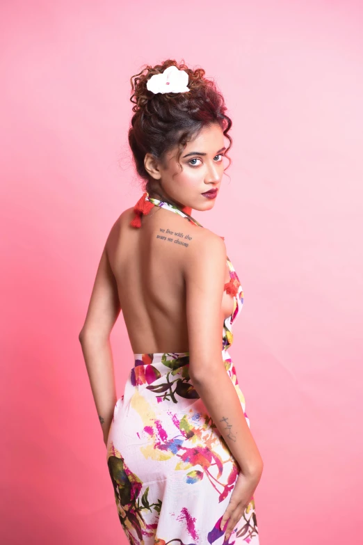 the back of a woman with a piece of hair in her hair, standing in front of a pink wall