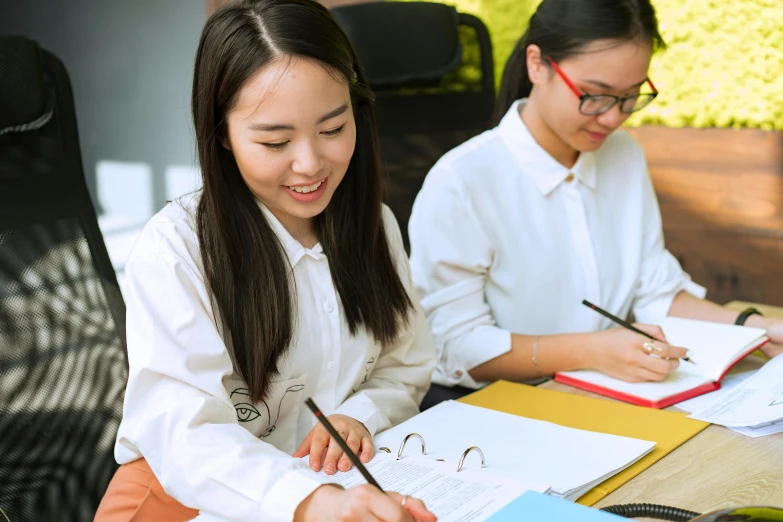 two young women at an office desk writing in notebooks