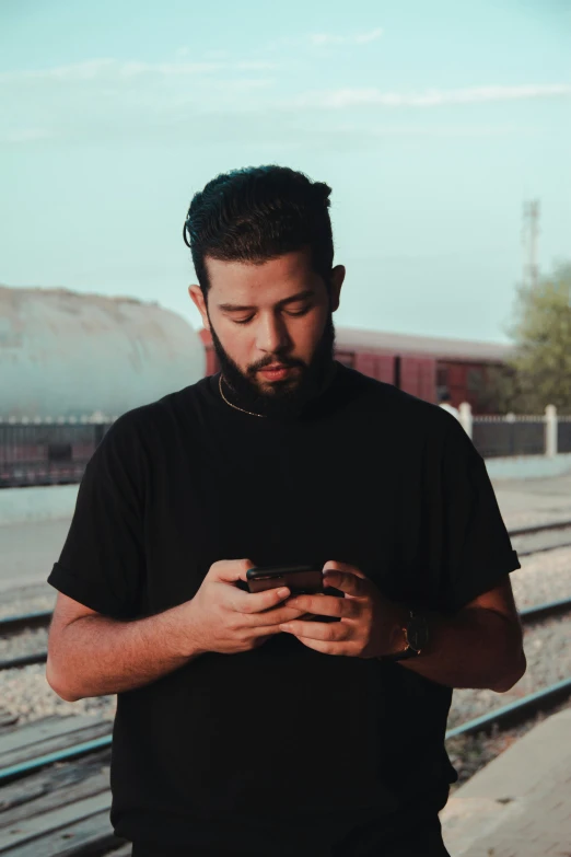 a man standing by some train tracks and looking at his cellphone