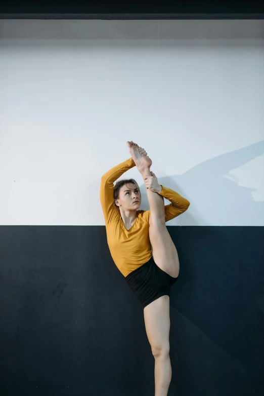 a woman is standing in the air wearing tight black pants and a gold shirt