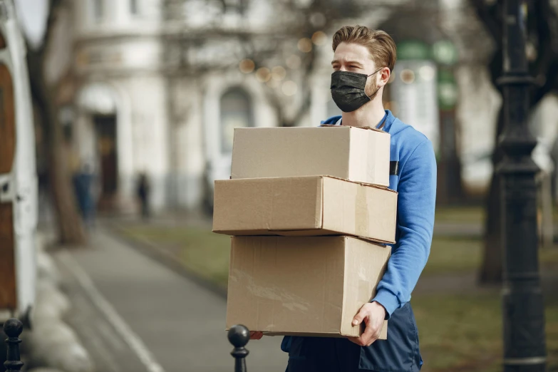 man holding boxes wearing a face mask on the street