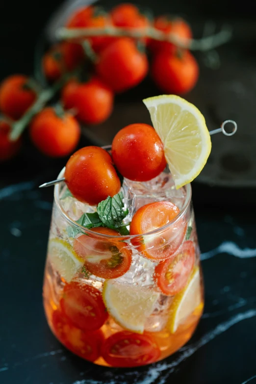 a clear glass with ice water and cherry tomatoes and lemon wedges