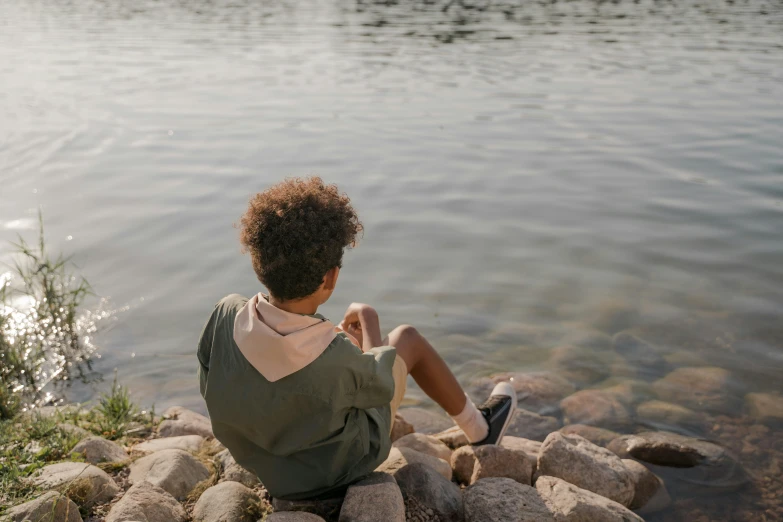 the  is sitting alone on rocks by the water