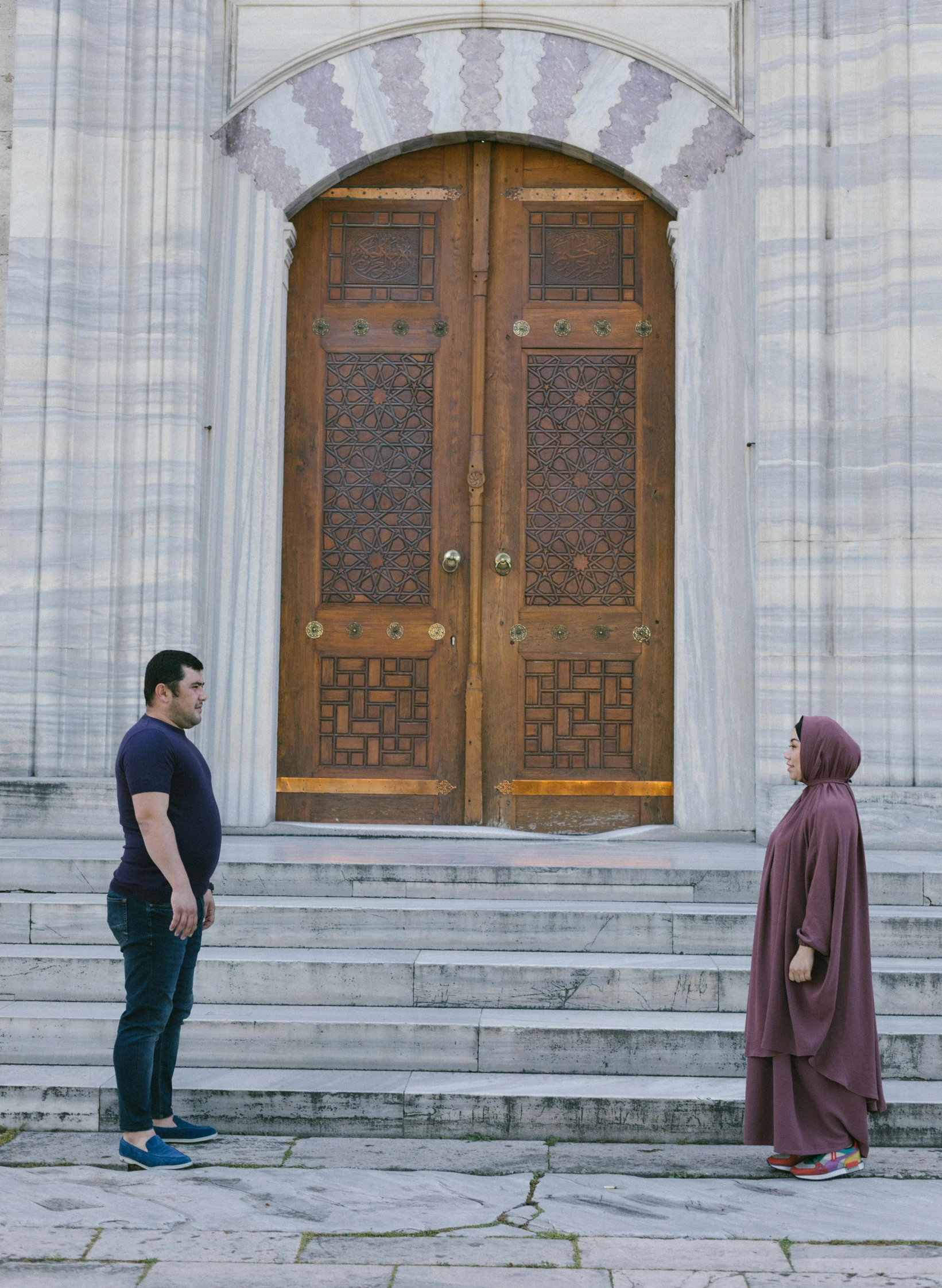 two muslim people standing outside an ornate wooden door