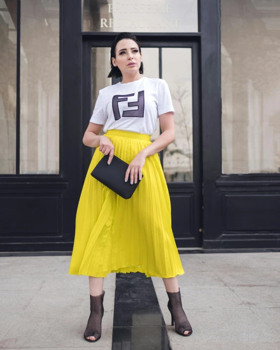 the young lady in a white shirt, yellow pleaed skirt and black heels is holding an envelope