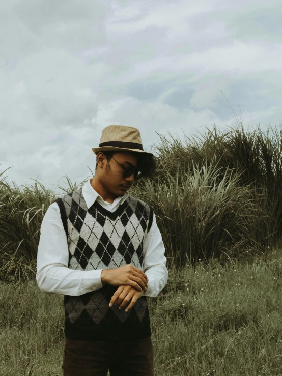 man standing in a field with a sweater vest and hat on