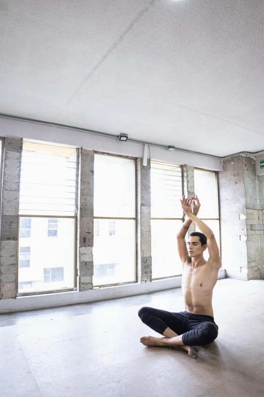 a shirtless man doing a yoga pose in an empty room