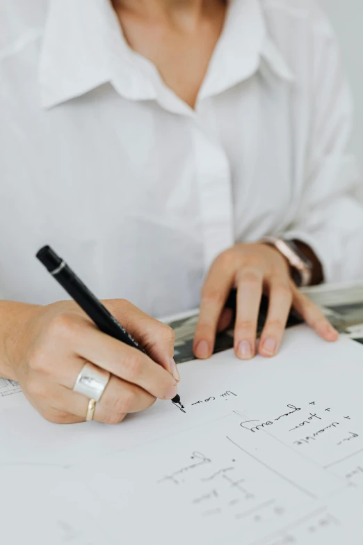 a woman in white shirt sitting at table with pen and paper