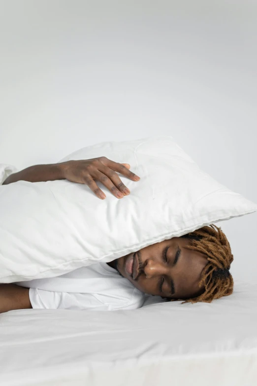 a woman lying in bed hiding under a pillow