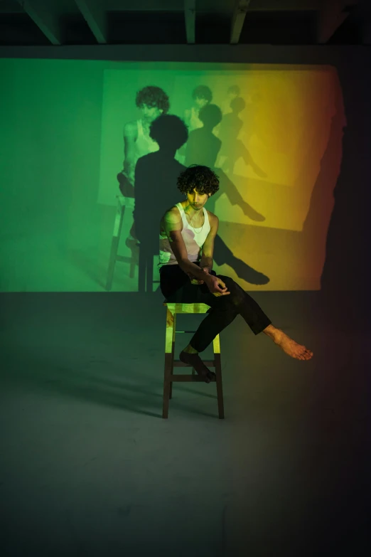 a man sits on a chair, with the shadow of people across the room