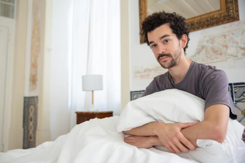 a man with curly hair holding a large pillow