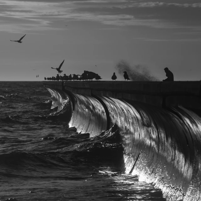 the waves are close to a concrete barrier that extends into the ocean and people stand on it