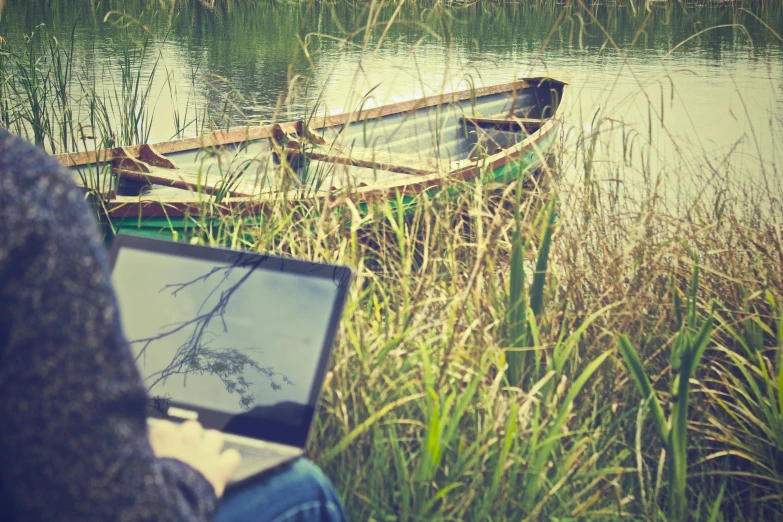 the person uses their laptop to view a boat on the river