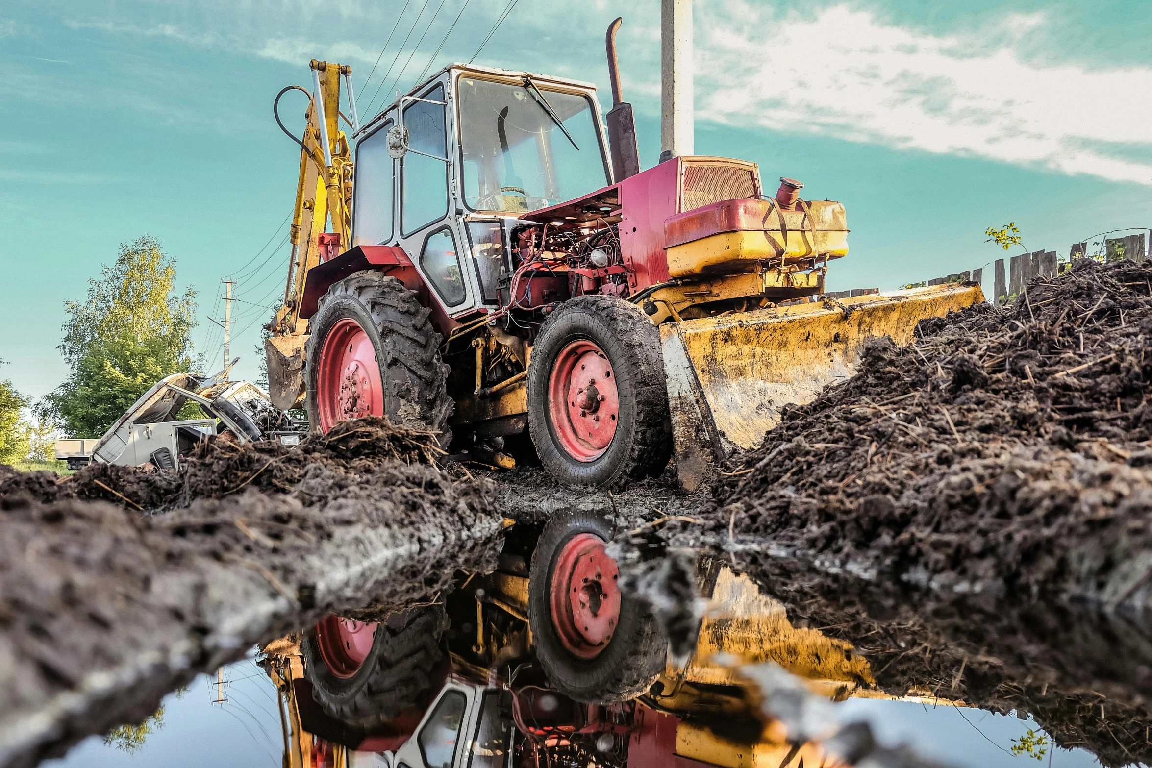 a red and yellow tractor sits in mud by some water