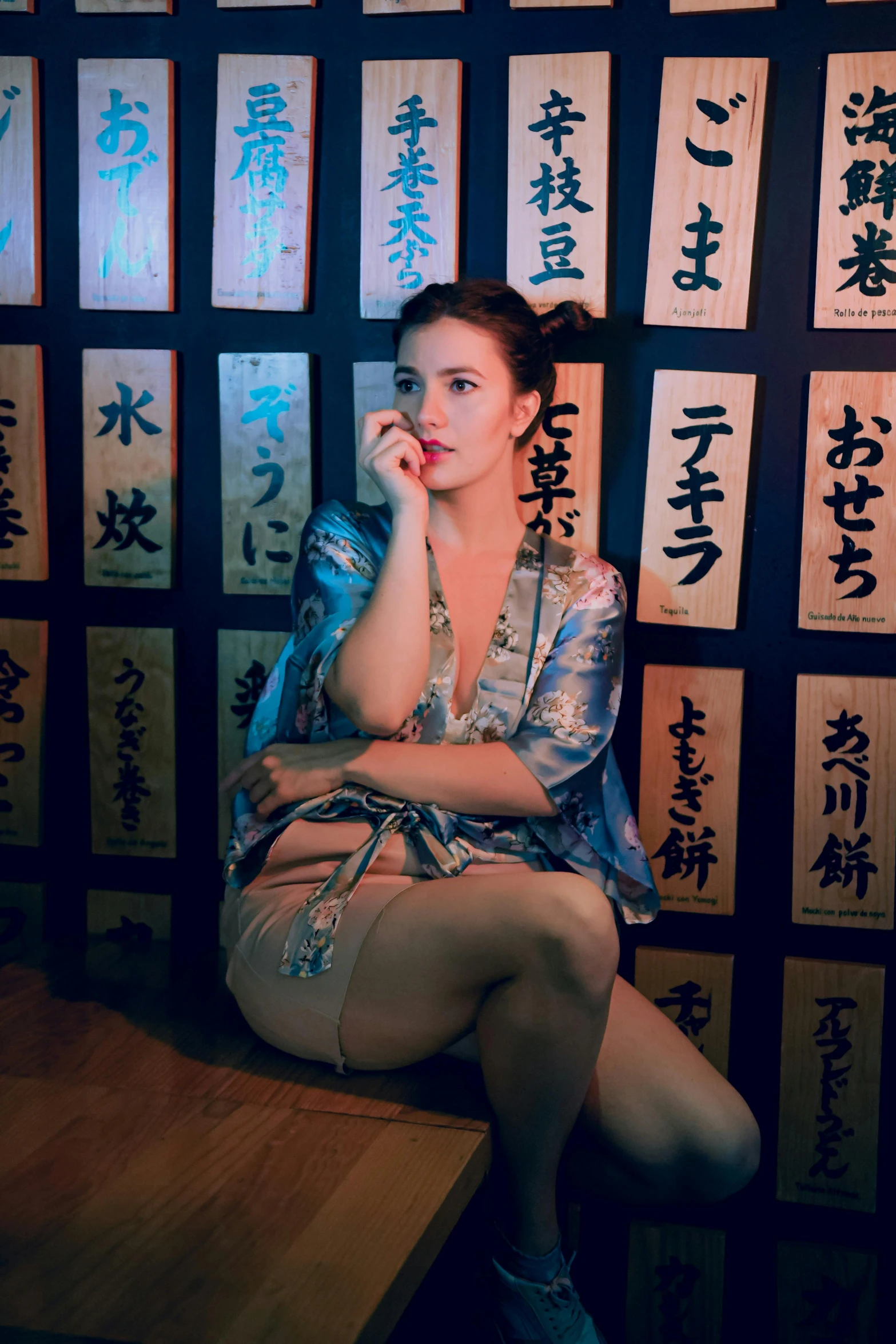 a woman sitting on top of a wooden table next to a wall with japanese calligraphy