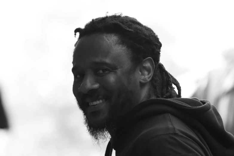 man with dreadlocks smiling while holding onto a cell phone