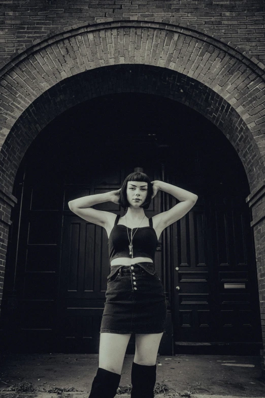 black and white po of a woman in short skirt standing in front of brick arch