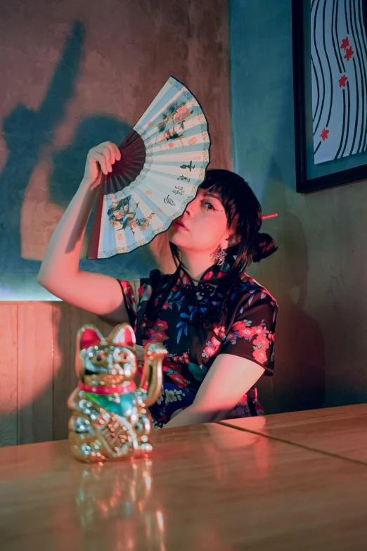 a young lady sitting in front of a table holding an oriental style fan